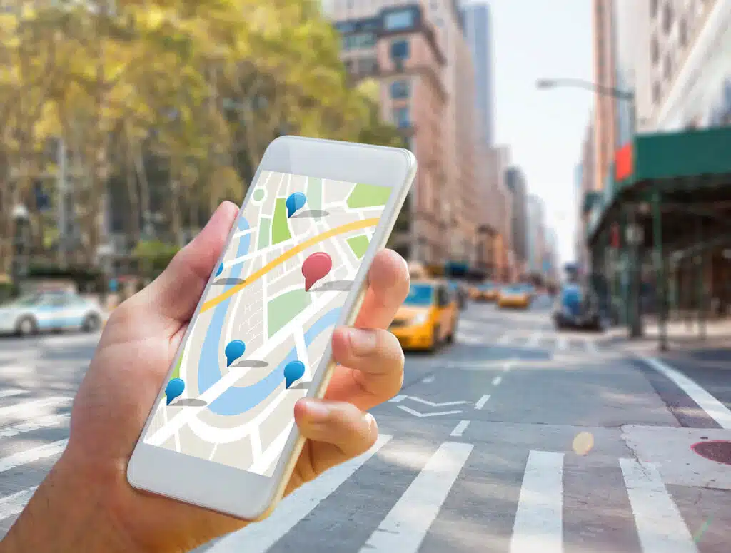 Person hält Smartphone mit digitaler Karte in urbaner Umgebung.